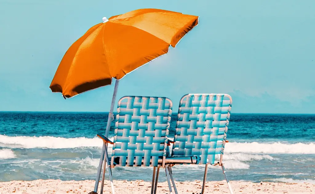 Vacation Aquarium Care - Two blue and white beach stools on the sand with an orange beach umbrella providing shade 