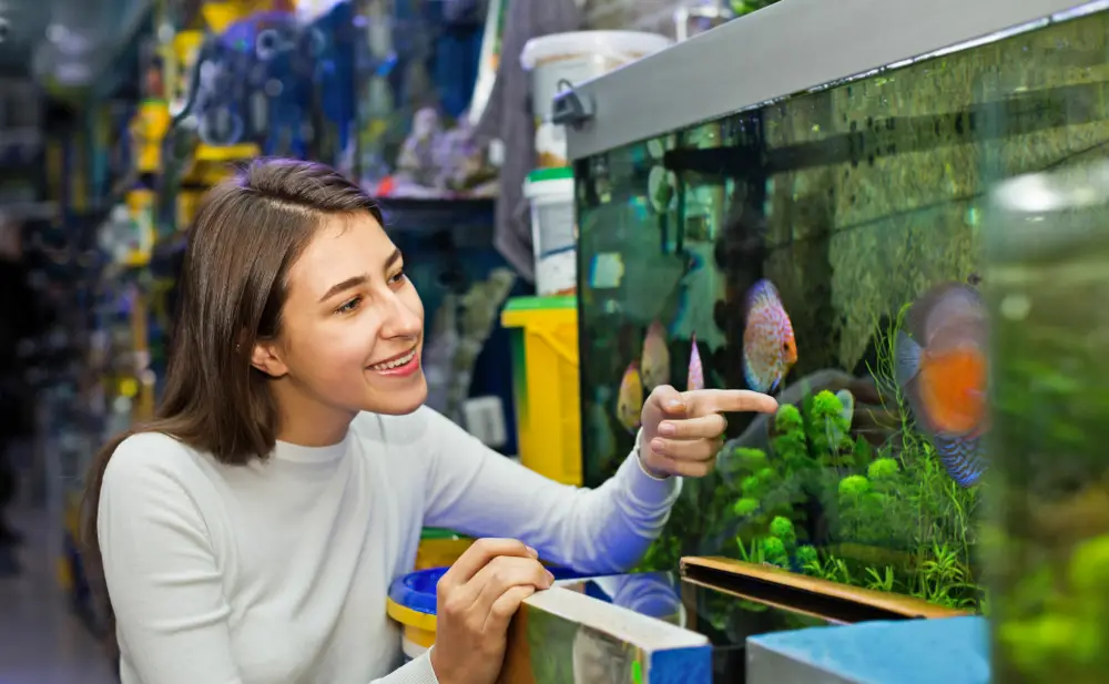 ips for Choosing the Right Fish — A young smiling woman looks at the aquarium fish at the pet store.