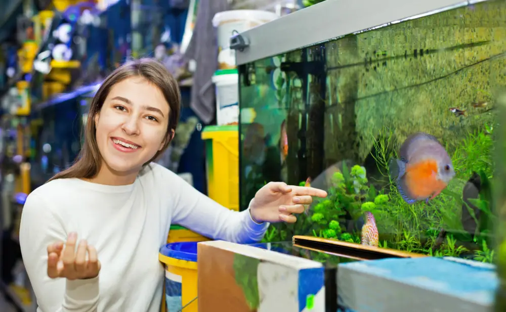 Choosing the Right Fish — A young smiling European girl looking at aquarium fish at the pet store. 