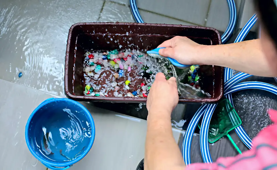Clean an Aquarium Sump — A person squatting and cleaning and scrubbing their aquarium equipment